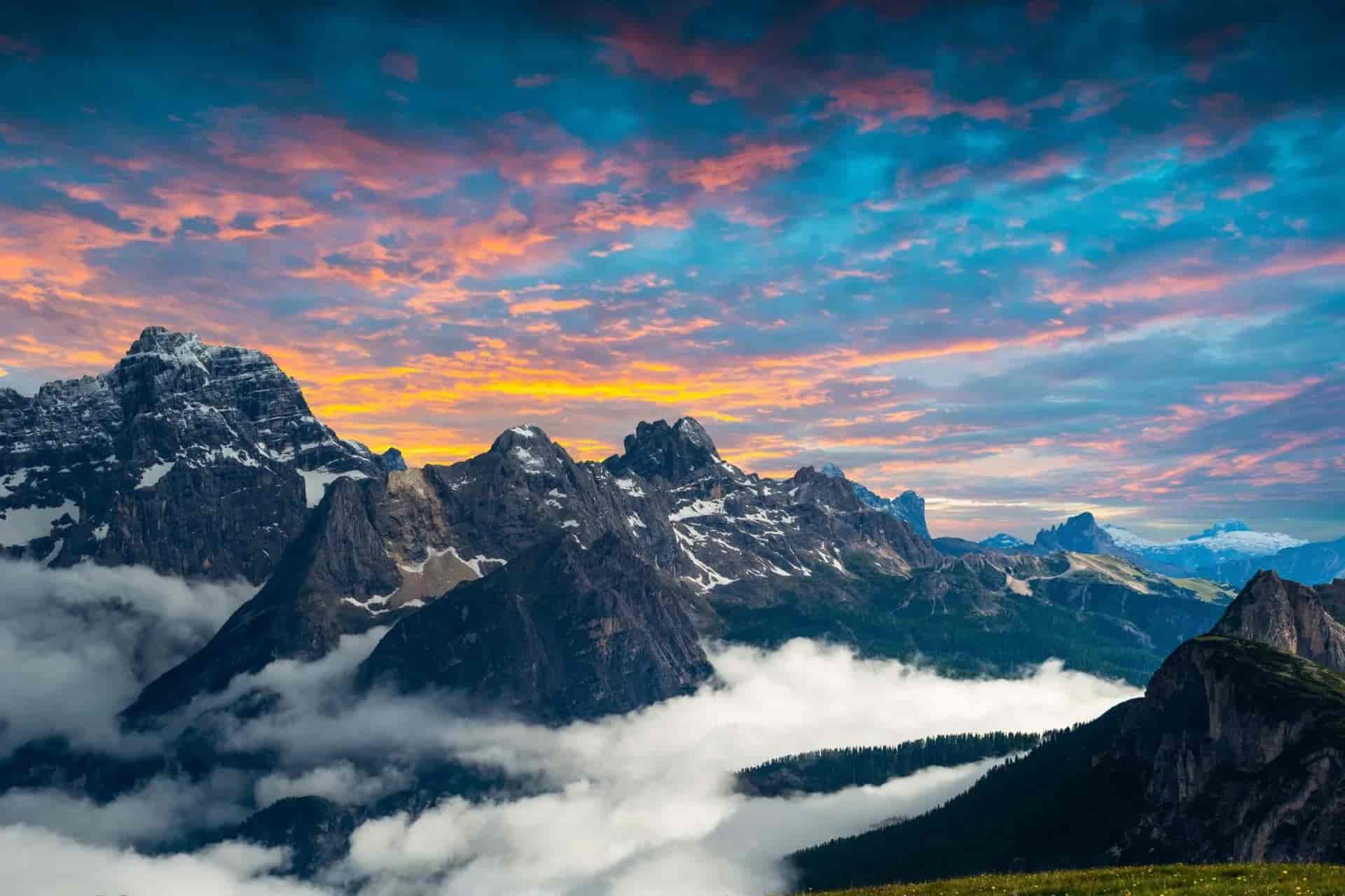 Dolomites mountains with snow patches above clouds at sunrise with pink and blue sky