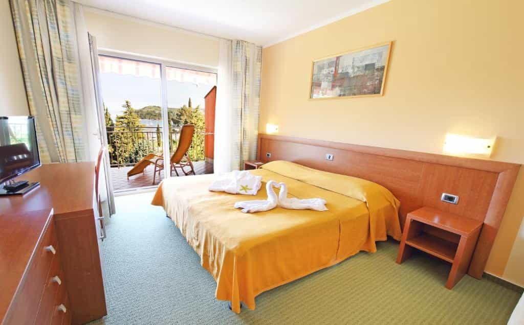 Hotel room with yellow bedspread, towel swans, and balcony view of trees and water.
