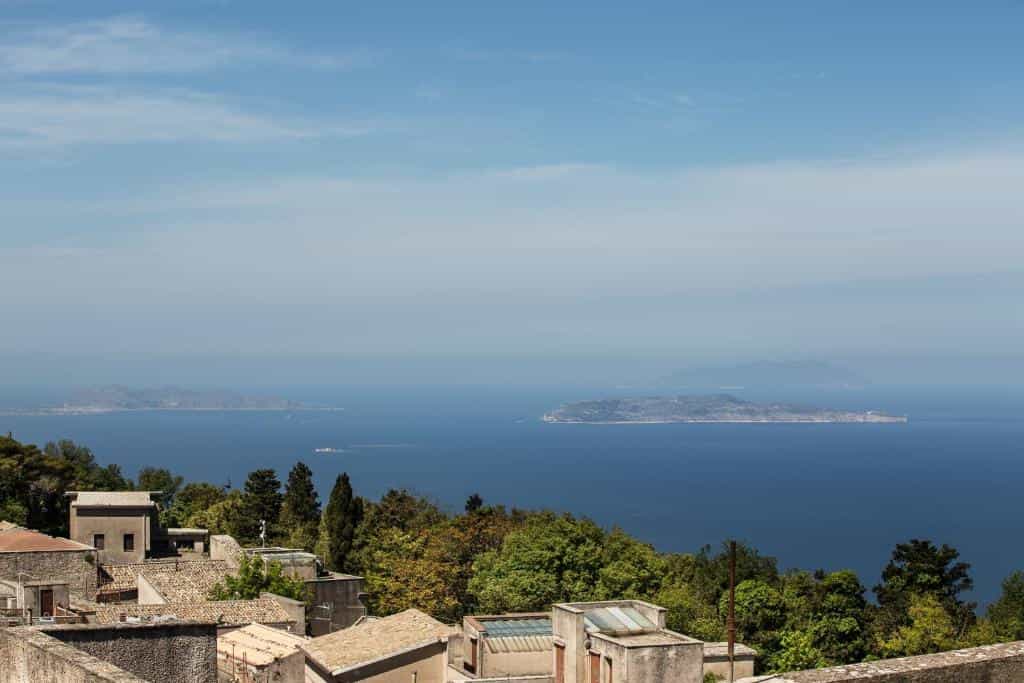 Coastal town rooftops overlooking the blue sea with distant islands under a bright sky.