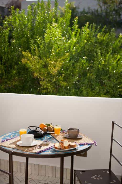 Breakfast setting with cake, juice, and tea on a tiled balcony overlooking green foliage in Favignana.