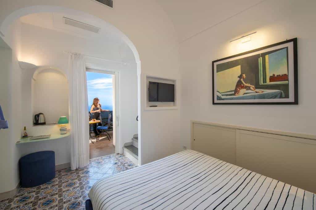Boutique hotel room with striped bedding, artwork, and balcony view of the sea.