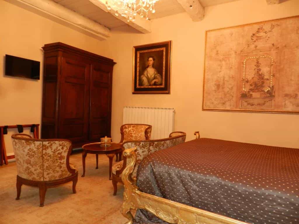 Bedroom with ornate gold bed, antique wooden wardrobe, and floral upholstered chairs