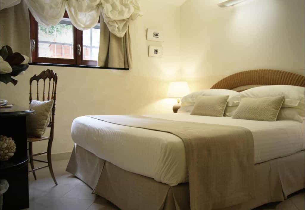 Bedroom with large bed, wicker headboard, and window with draped curtains at Locanda A Cà Du Gigante.