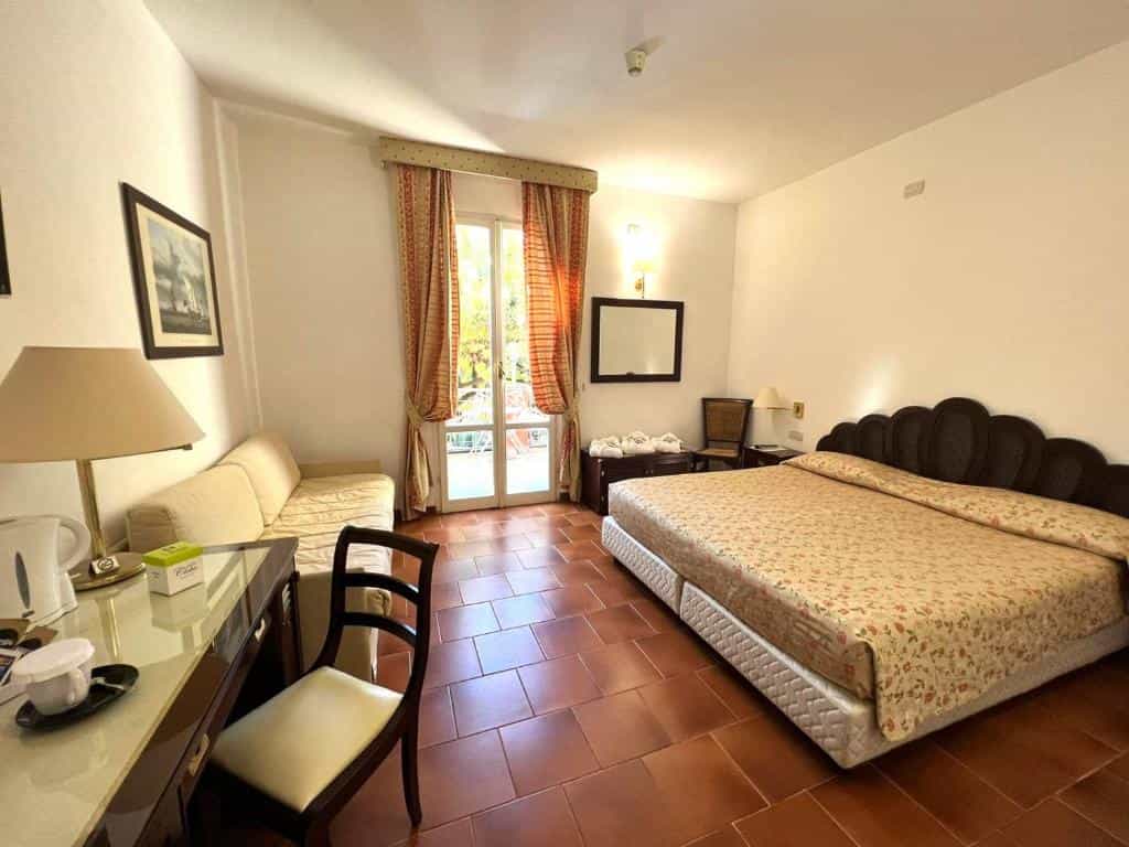 Hotel room with large bed, desk, sofa, and balcony doors with patterned curtains