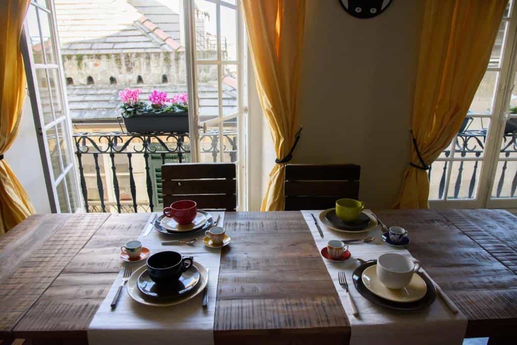 Breakfast setting for two on rustic wooden table by balcony with pink flowers.