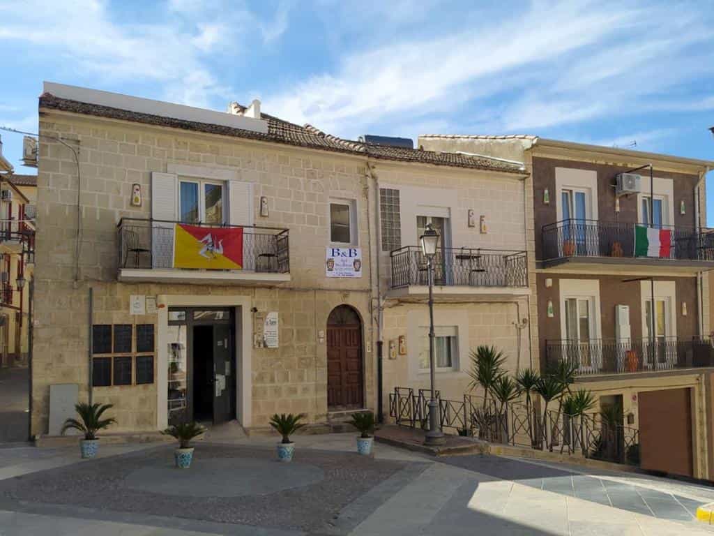 Stone buildings with balconies, Sicilian and Italian flags, in Acquaviva-di Vullo square.