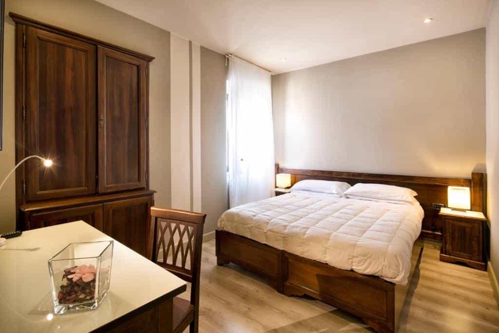 Hotel bedroom with wooden furniture, white bedding, and desk illuminated by lamps.