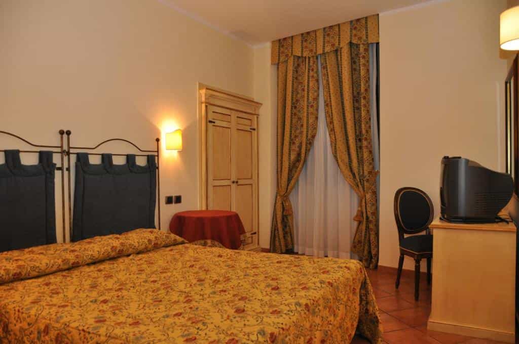 Hotel room with yellow floral bedspread, dark headboard, and patterned gold curtains.