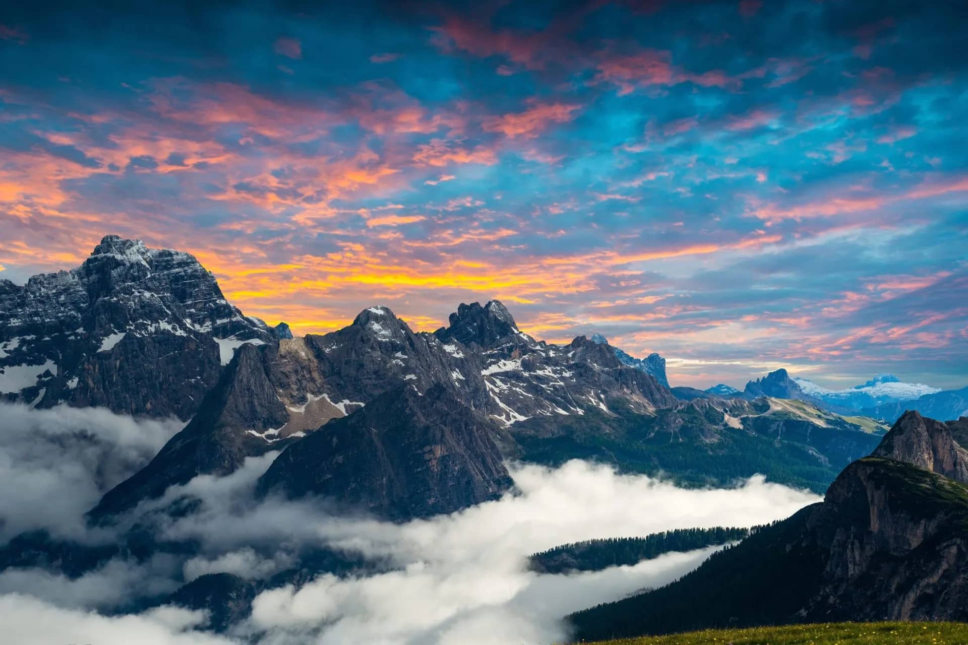 Dolomites mountains with snow patches above clouds at sunrise with pink and blue sky