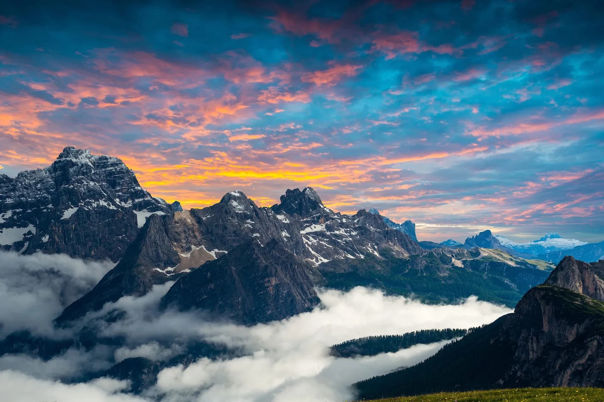 Rugged mountain peaks with snow and fog at sunrise under a dramatic pink and blue sky in the Dolomites.