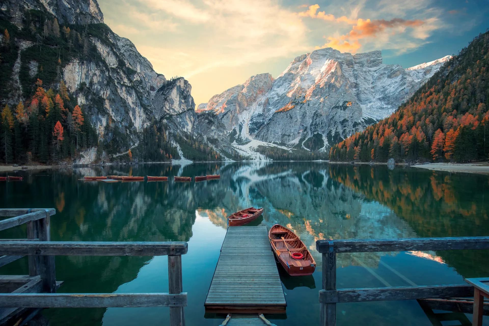 Wooden rowboats docked at a pier on Lago di Braies with mountains and autumn trees reflected.