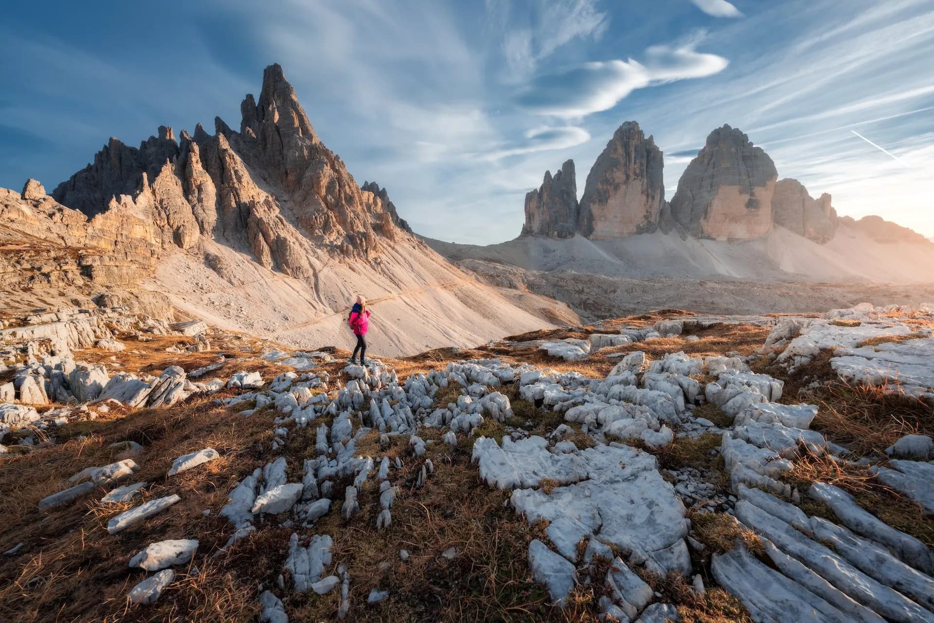 Hiker overlooking Tre Cime di Lavaredo peaks in the Dolomites with rocky foreground.