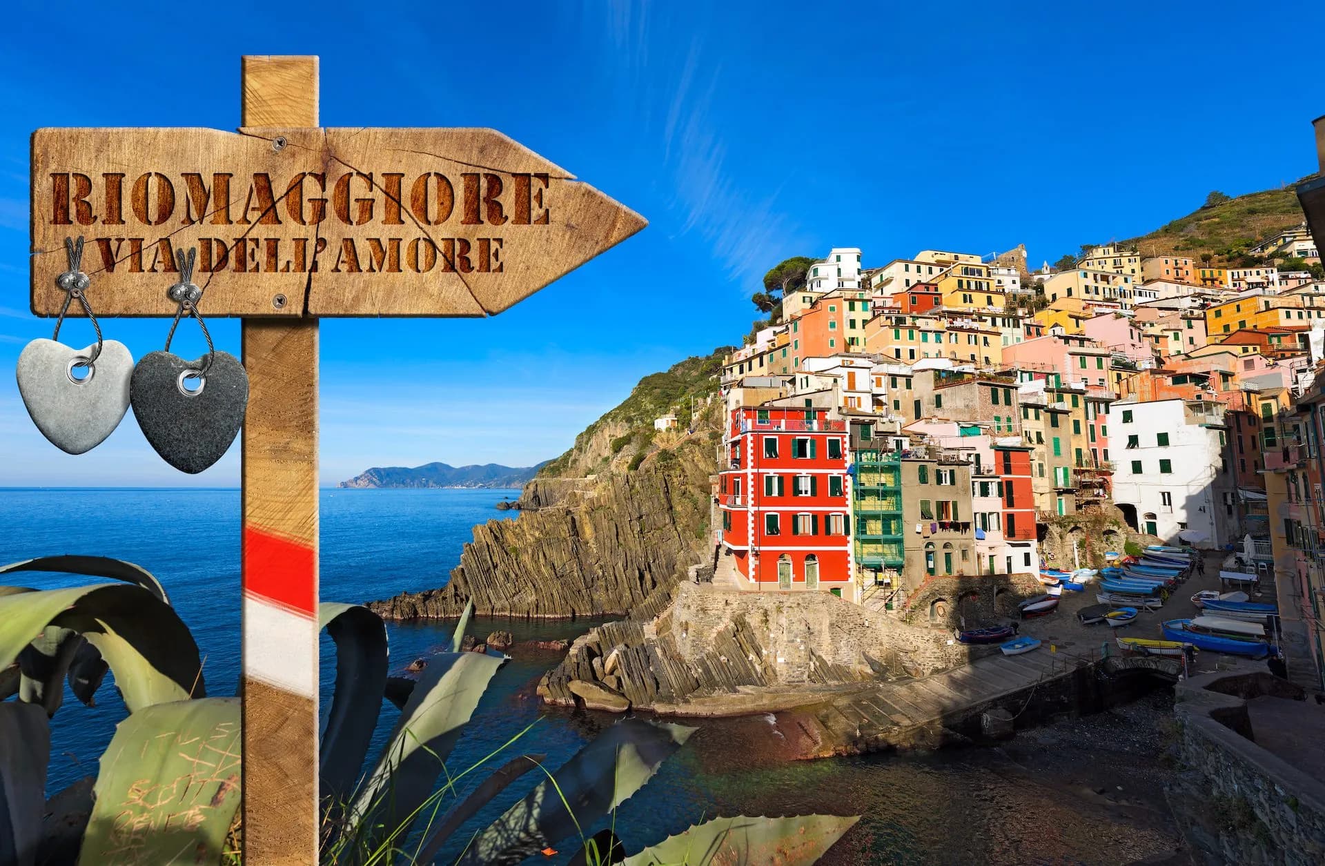 Riomaggiore Via dell'Amore signpost overlooking colorful cliffside houses and the sea.