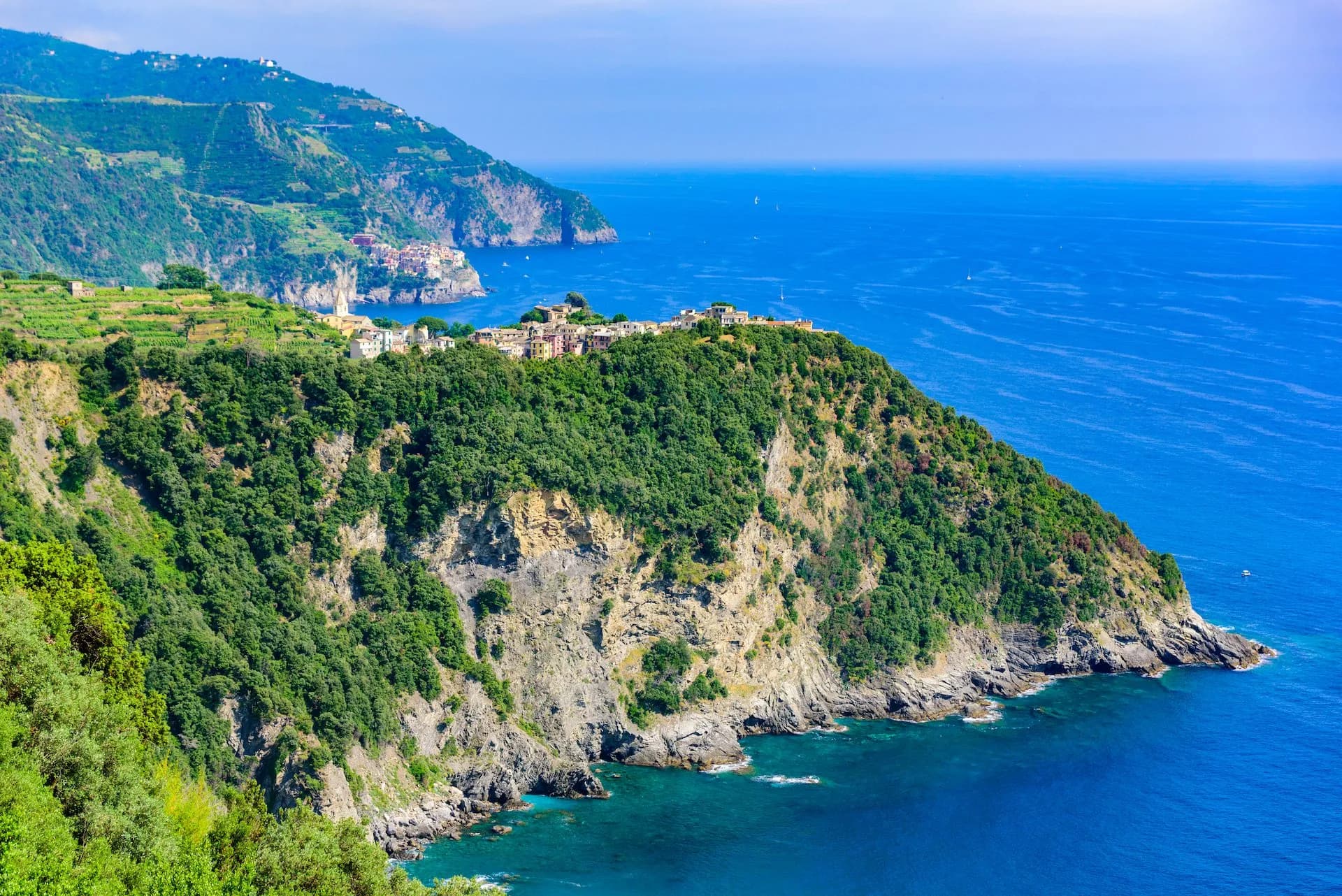 Coastal village perched on a steep, green cliff overlooking the deep blue Mediterranean Sea near Corniglia.