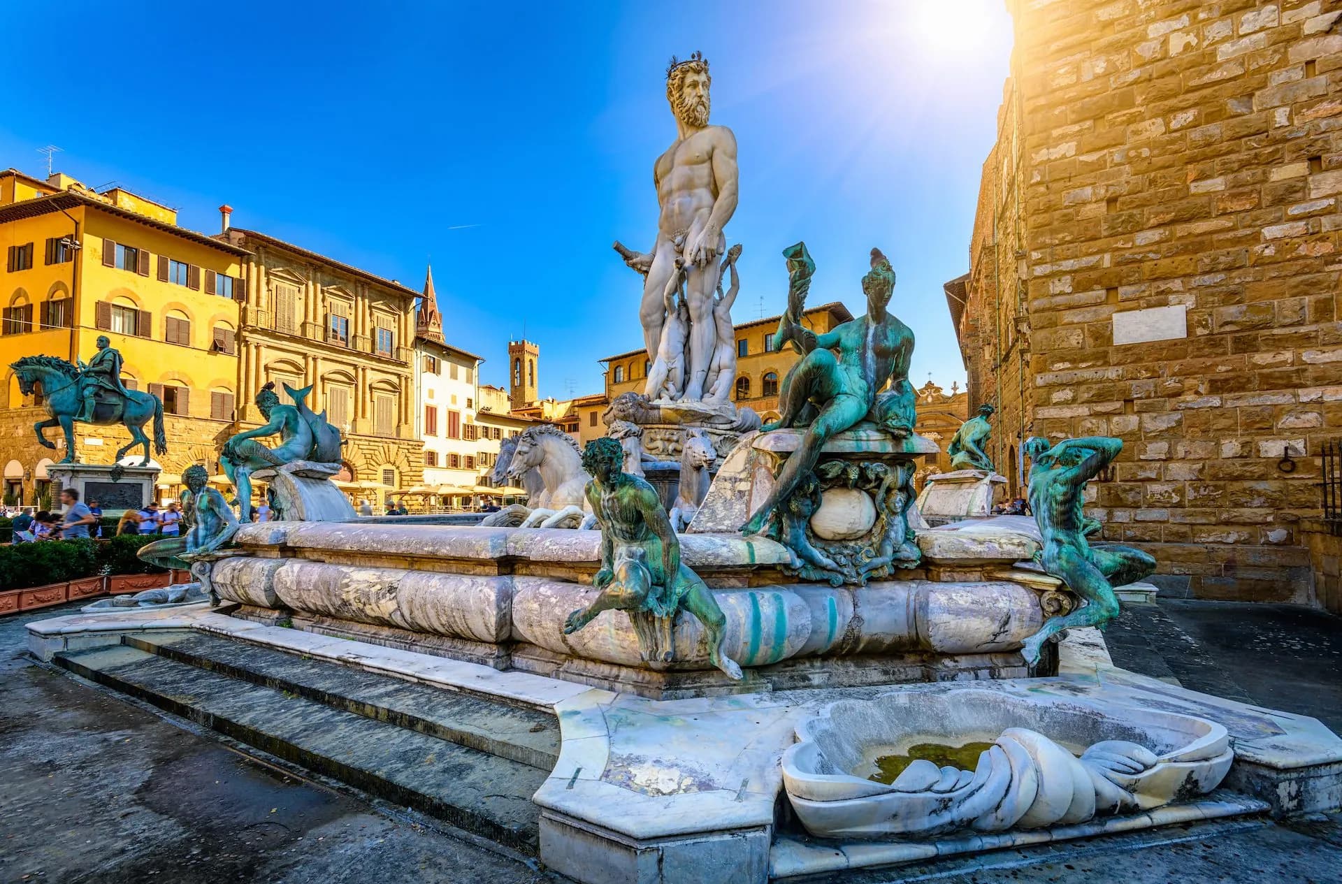 Fountain of Neptune statues in Piazza della Signoria with bright sun on historic buildings.
