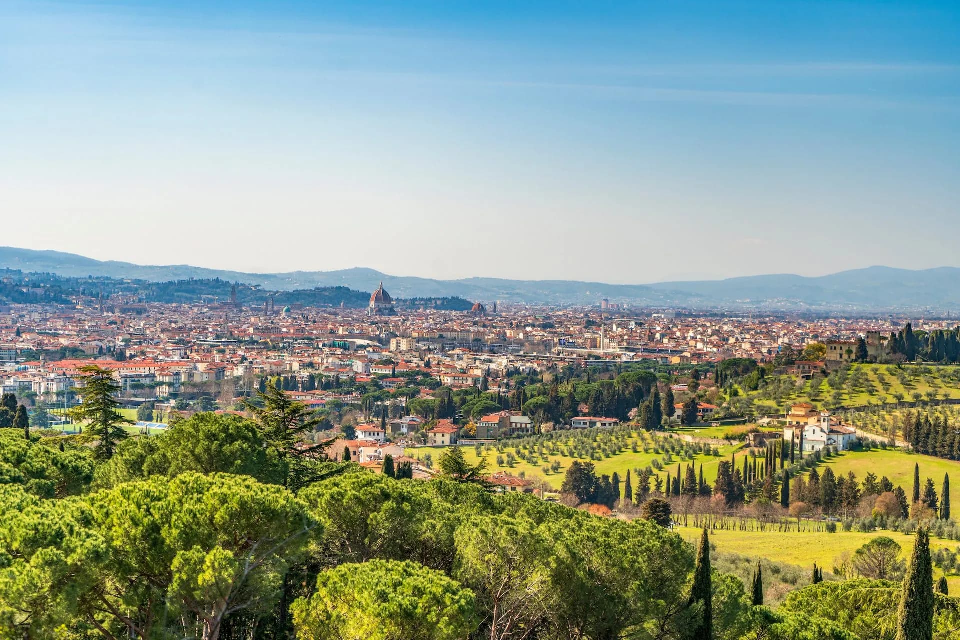 Panoramic view of Florence cityscape with Duomo dome, rolling hills, and green cypress trees.