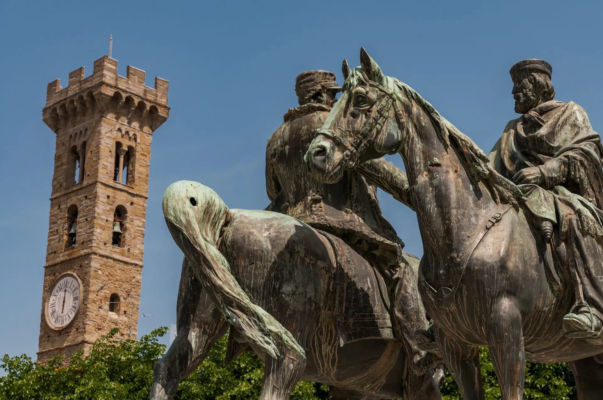 Equestrian bronze statue in front of stone clock tower under clear blue sky in Fiesole.