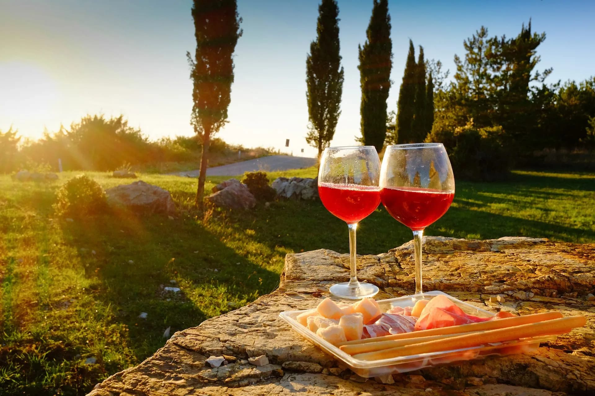 Two glasses of red wine and charcuterie on a stone surface in Tuscany at sunset