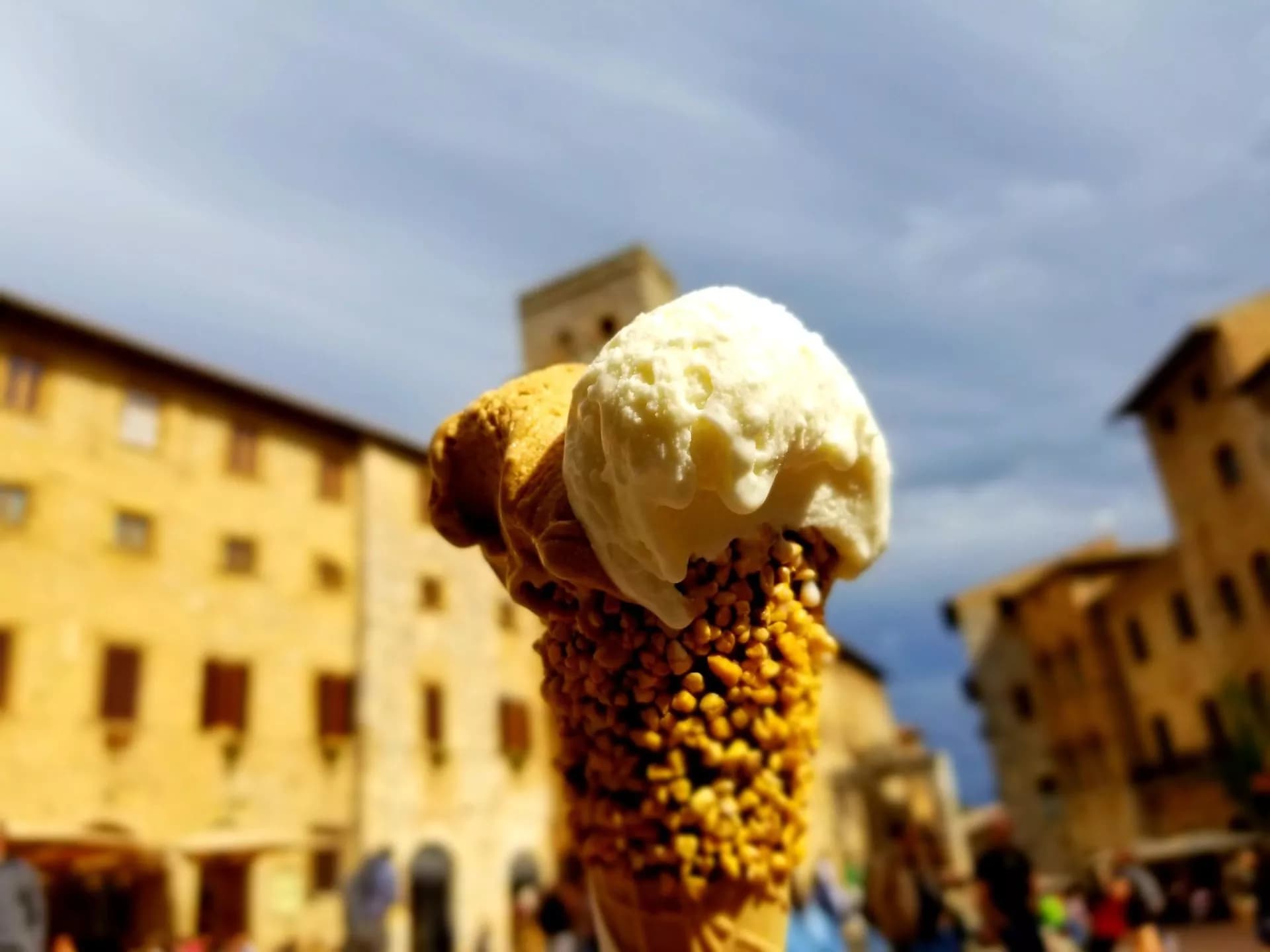 Gelato cone with nuts and white scoop against blurred historic buildings of San Gimignano.