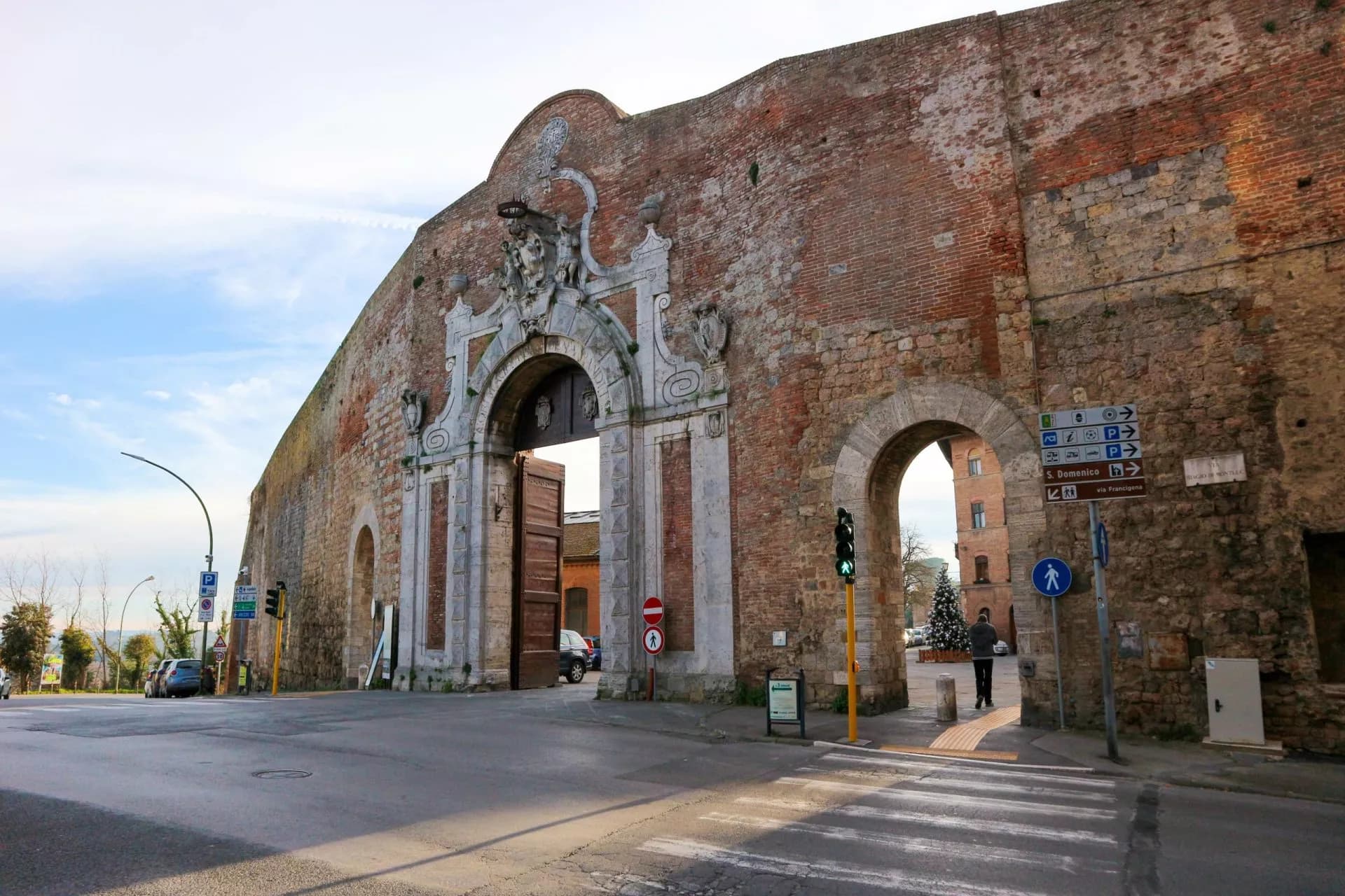 Porta Camollia, a large historic brick and stone gate in Siena, with traffic signals and street signs.