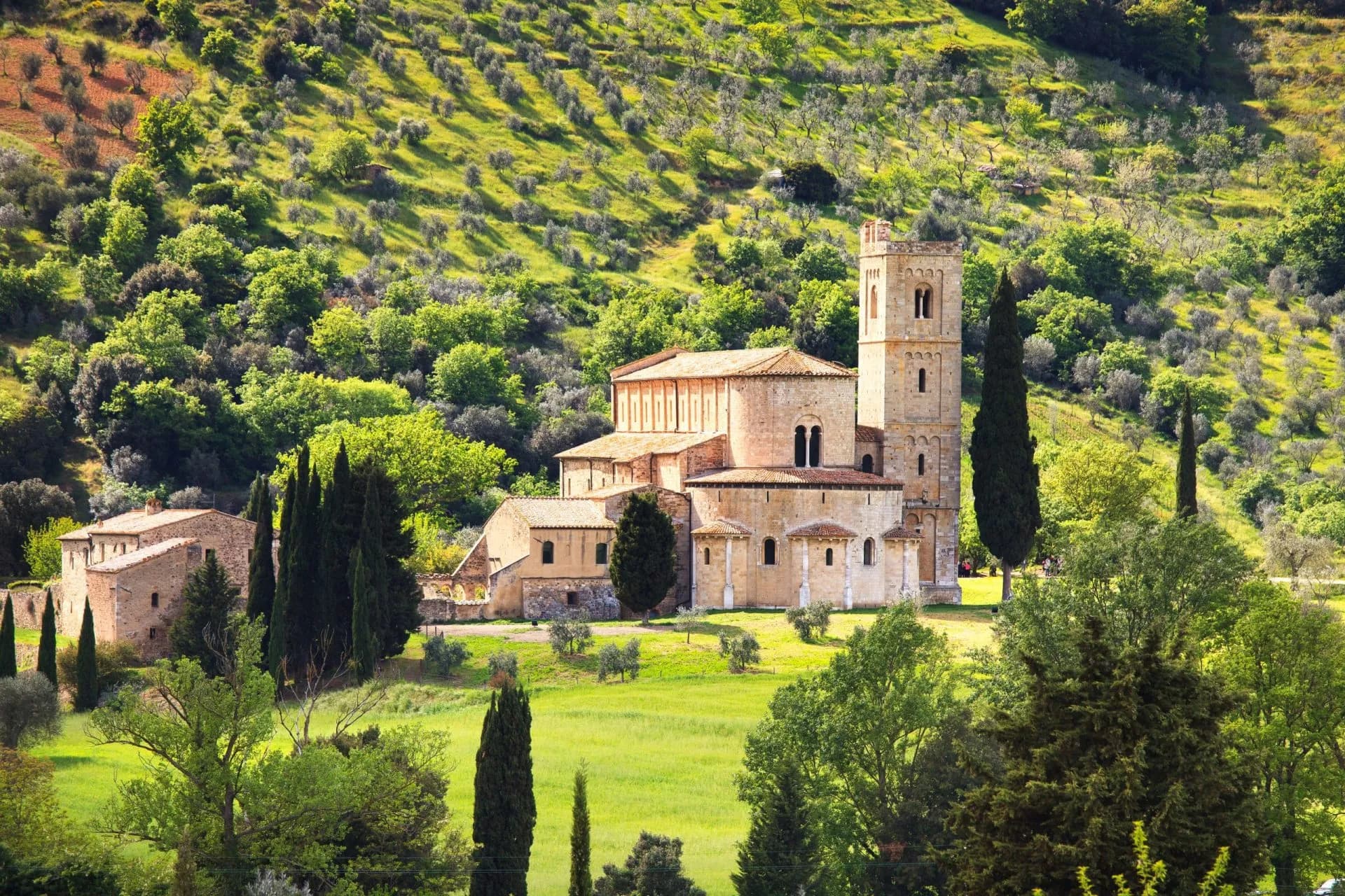 Sant'Antimo Abbey church surrounded by green hills and cypress trees in Tuscany, Italy