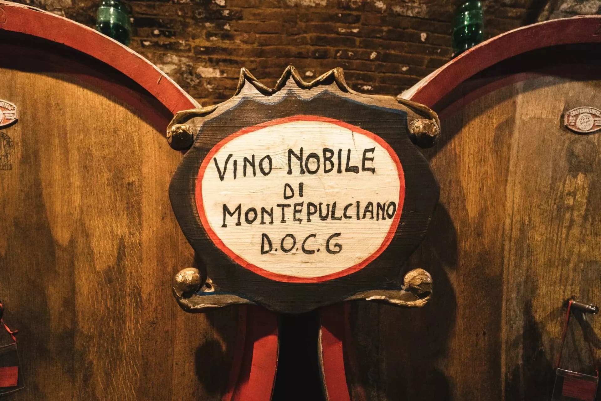 Sign reading "Vino Nobile di Montepulciano D.O.C.G." on large wooden wine barrels in a cellar.