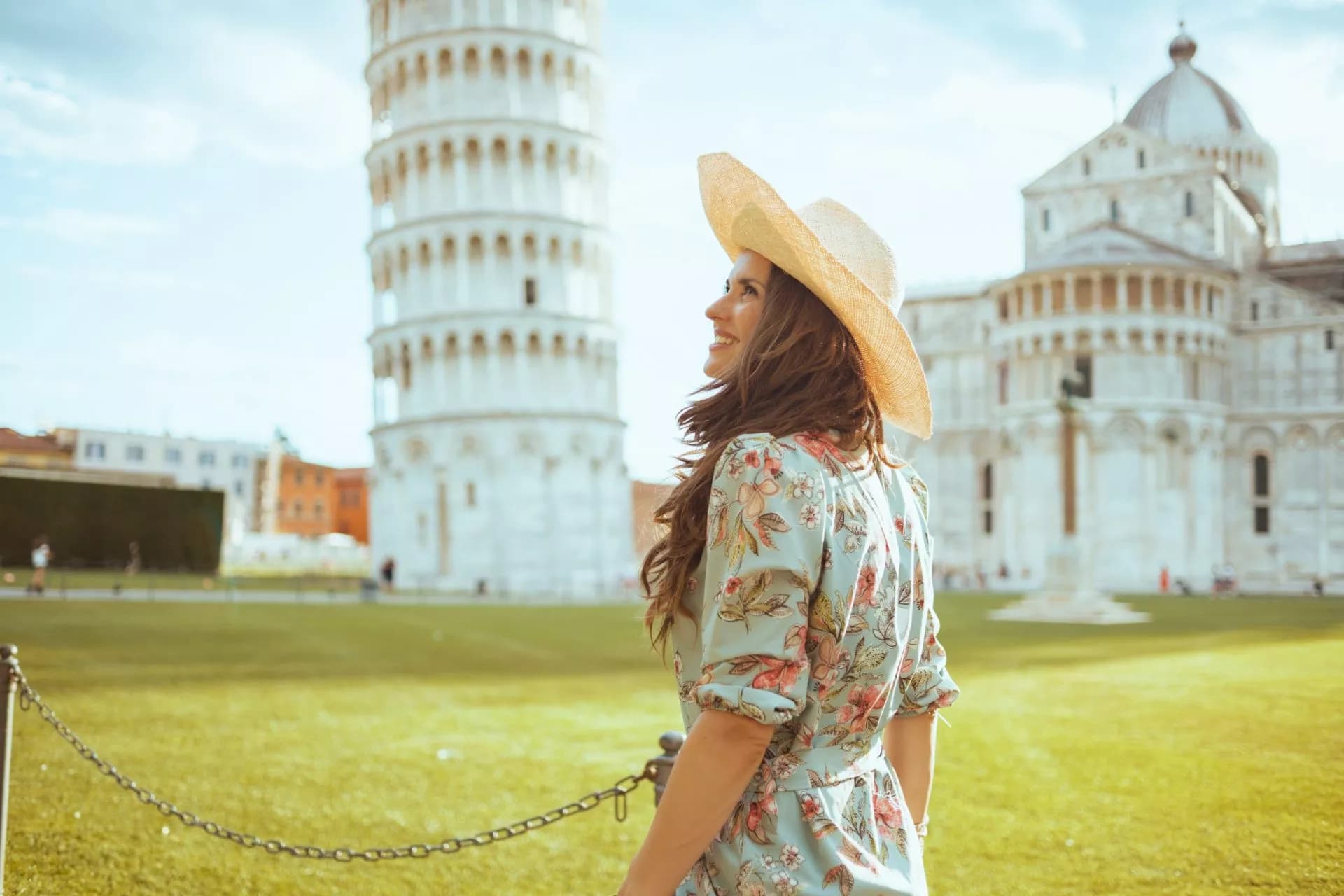 Woman in sun hat near Leaning Tower of Pisa and cathedral on sunny day