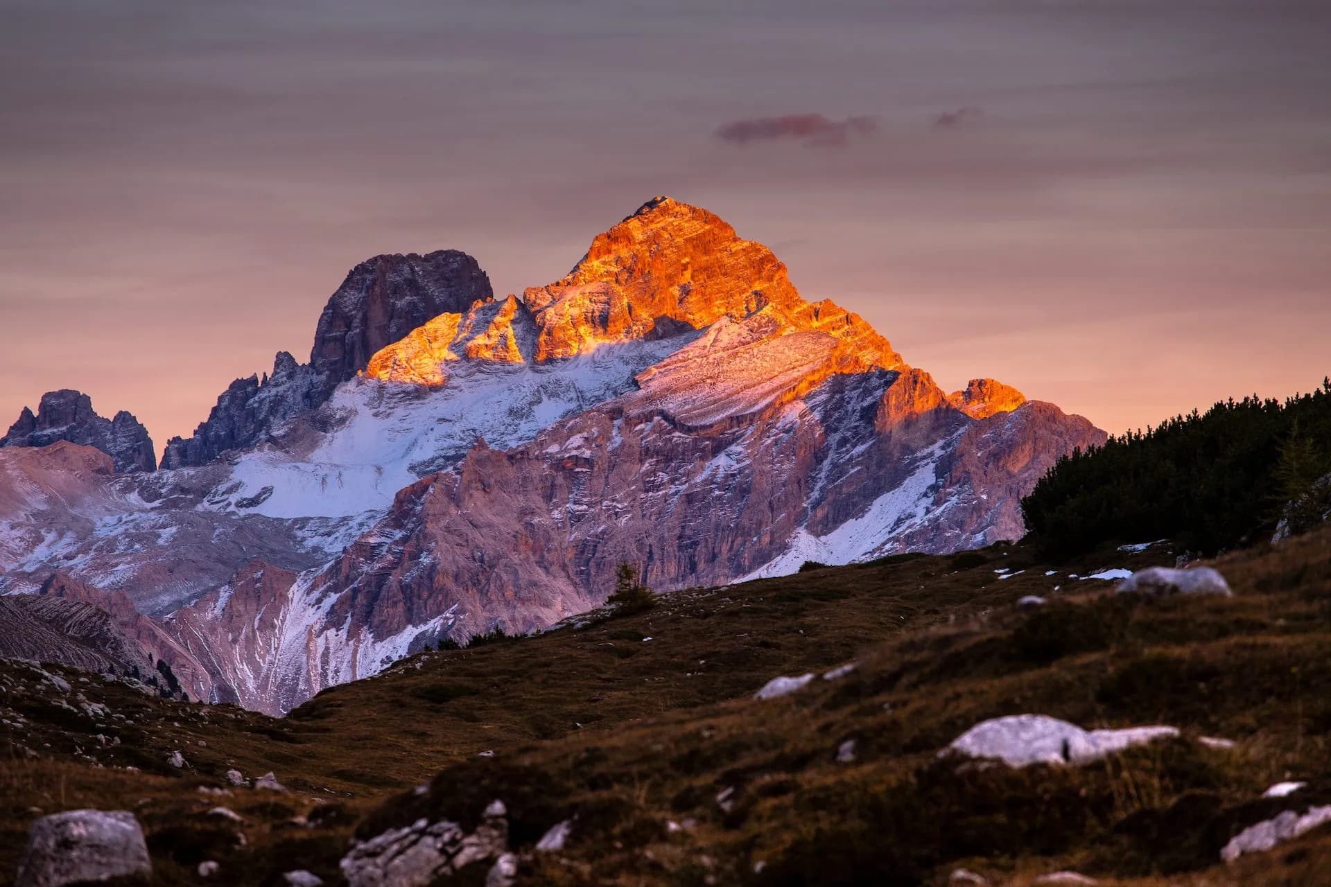 Alpine mountains with snow and golden sunrise light over foreground meadow at Rifugio Sennes.
