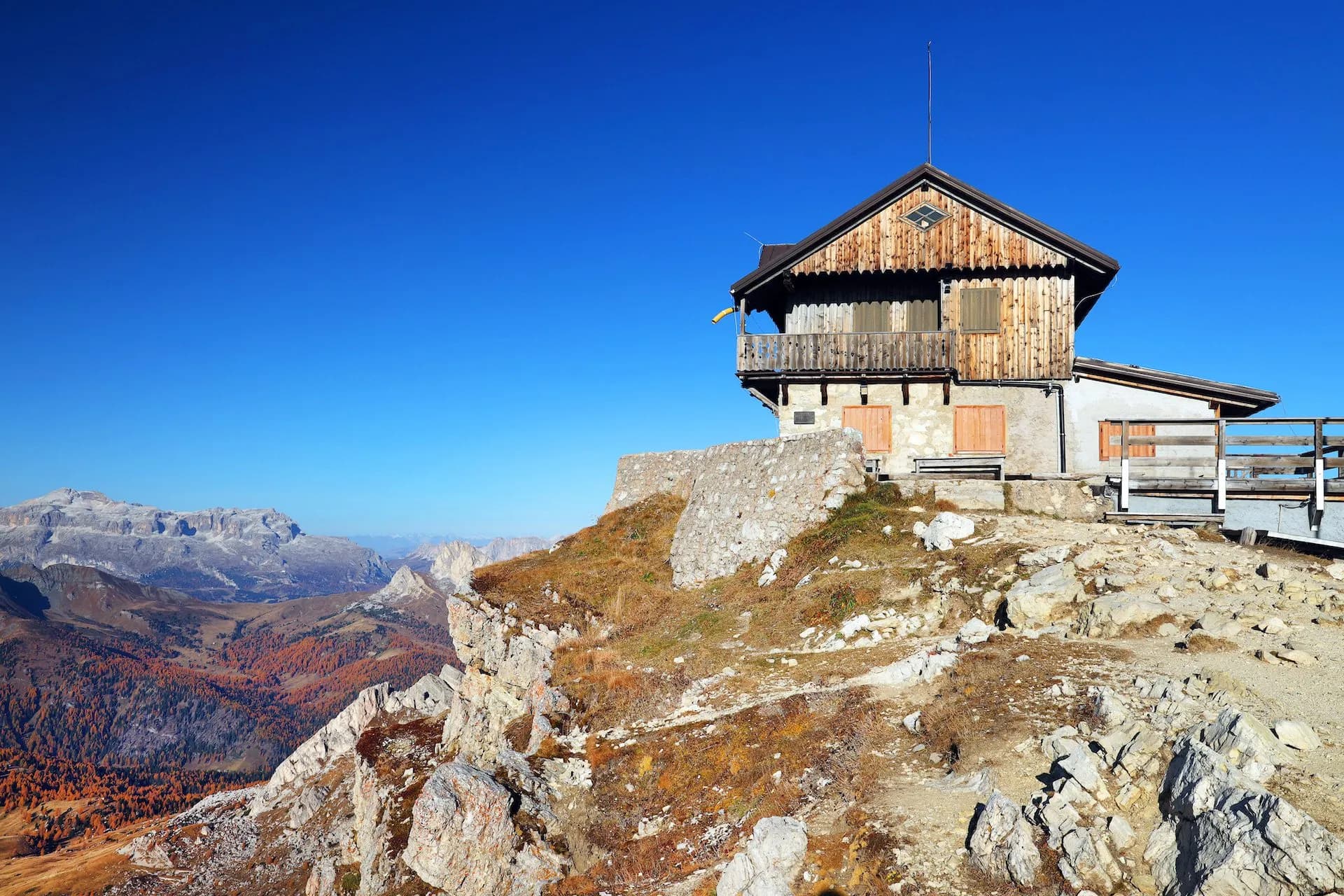 Rustic Rifugio Nuvolau mountain hut perched on rocky terrain with autumn colors in the valley below.
