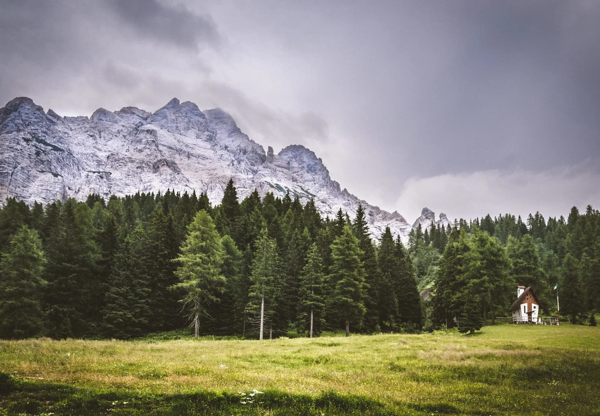 Mountain landscape with rocky peaks, pine forest, meadow, and small cabin near Passo Staulanza.