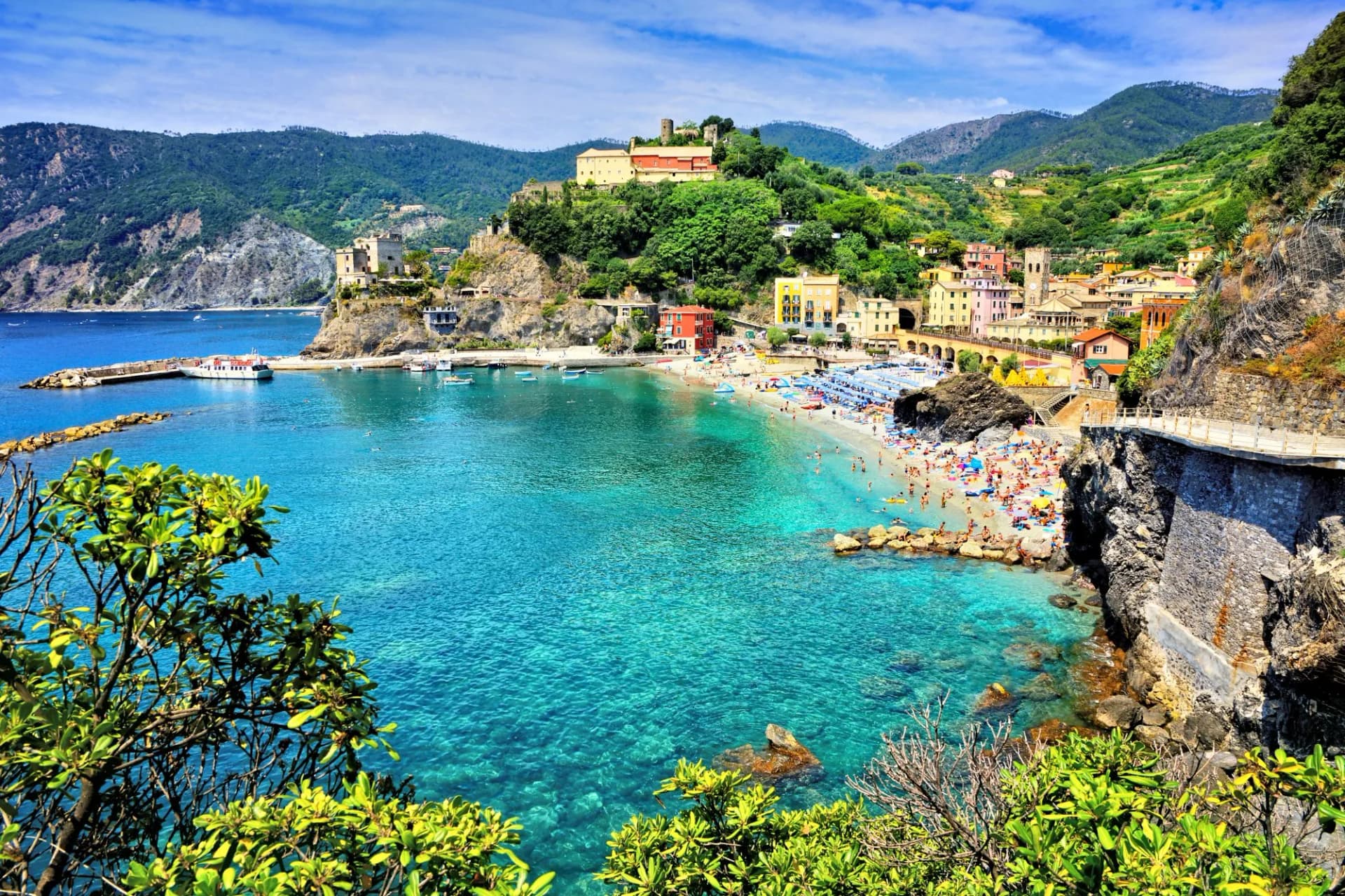 Beachgoers in Monterosso al Mare, Cinque Terre, with turquoise water and colorful hillside buildings.