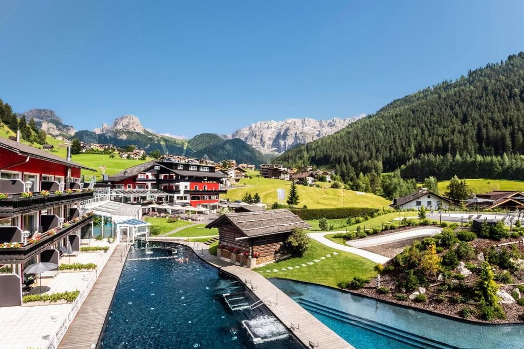Outdoor swimming pool at a resort in an alpine village with mountain peaks and green meadows.