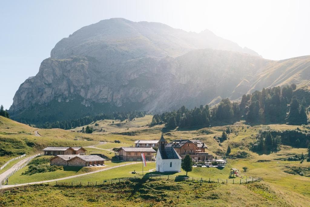 Small white chapel and wooden farm buildings in an alpine mountain meadow.