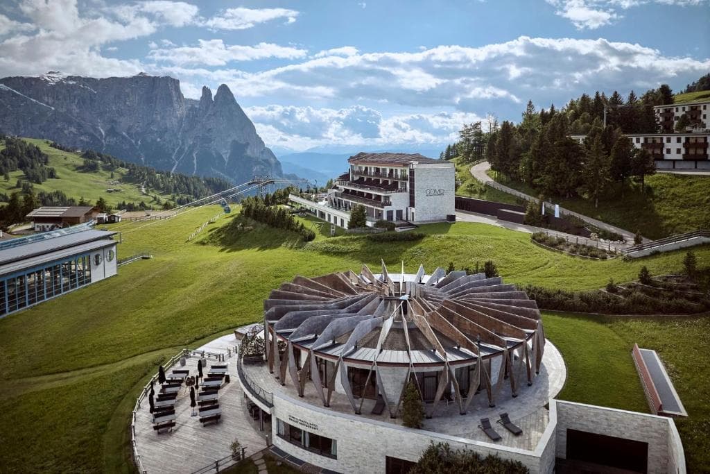 Modern hotel and circular restaurant building in the Dolomites mountain landscape with green meadows.