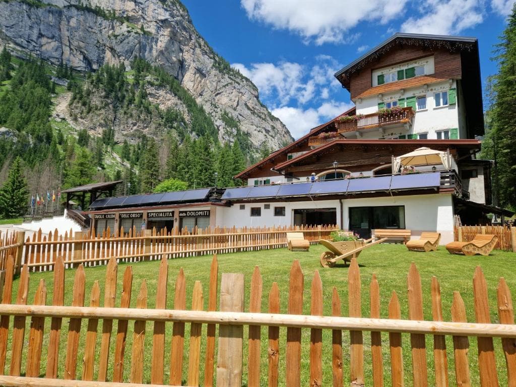 Alpine hotel with wooden balconies and lawn in front of a rocky mountain face.