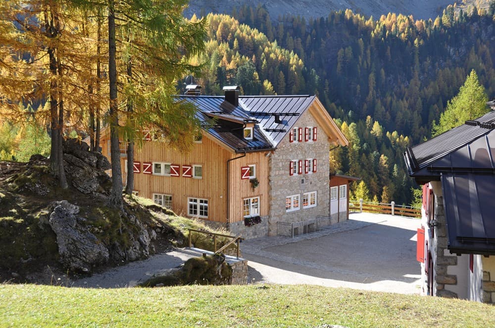 Alpine mountain lodge with stone and wood architecture surrounded by autumn forest.