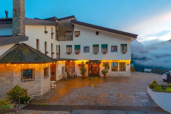 Alpine hotel building with stone courtyard and warm outdoor lighting at dusk.