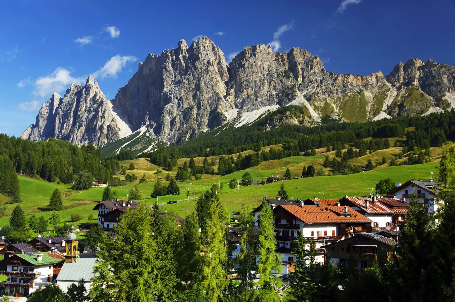 Alpine village with traditional houses below jagged mountains and green meadows in Cortina dAmpezzo surroundings.