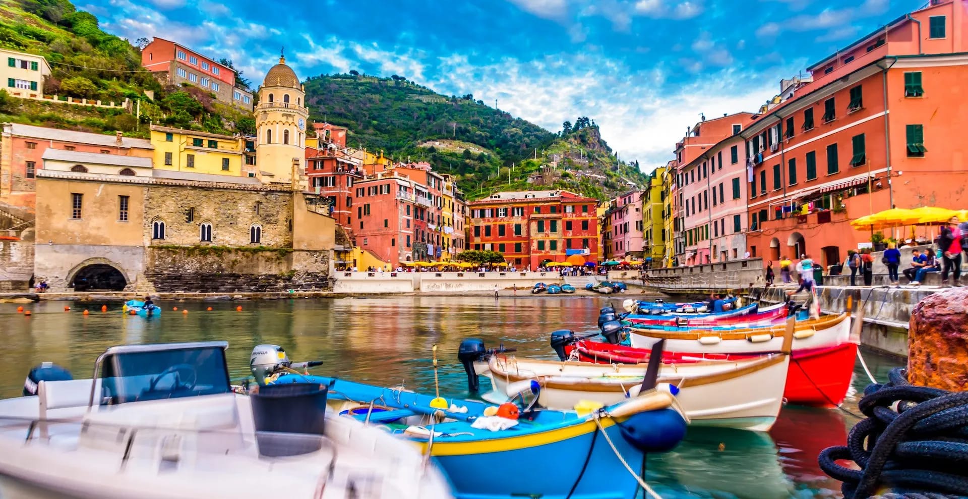 Colorful boats moored in harbor with colorful buildings and steep green hills of Vernazza.