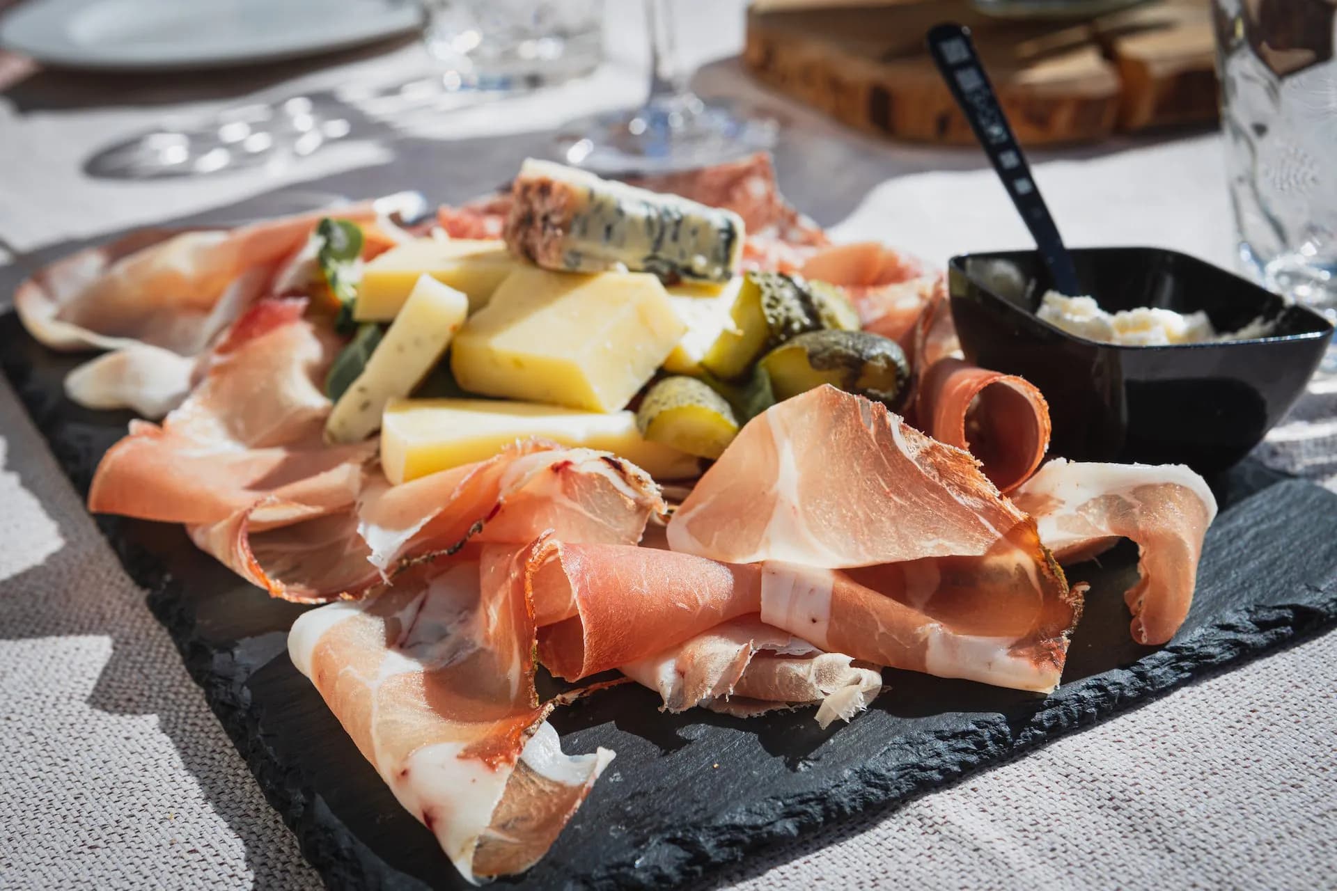 Charcuterie board with prosciutto, cheese, pickles, and dip on a slate platter in the Dolomites.