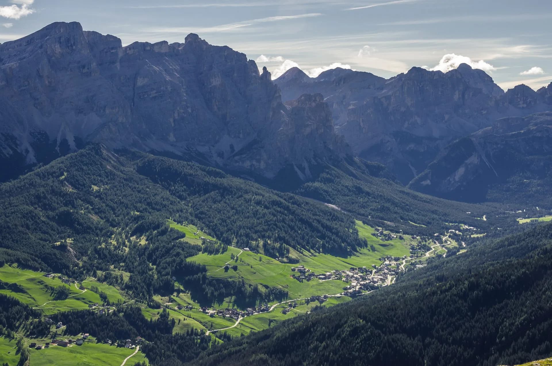 Alpine valley with village nestled between steep, dark mountains and green forested slopes, Val Badia.