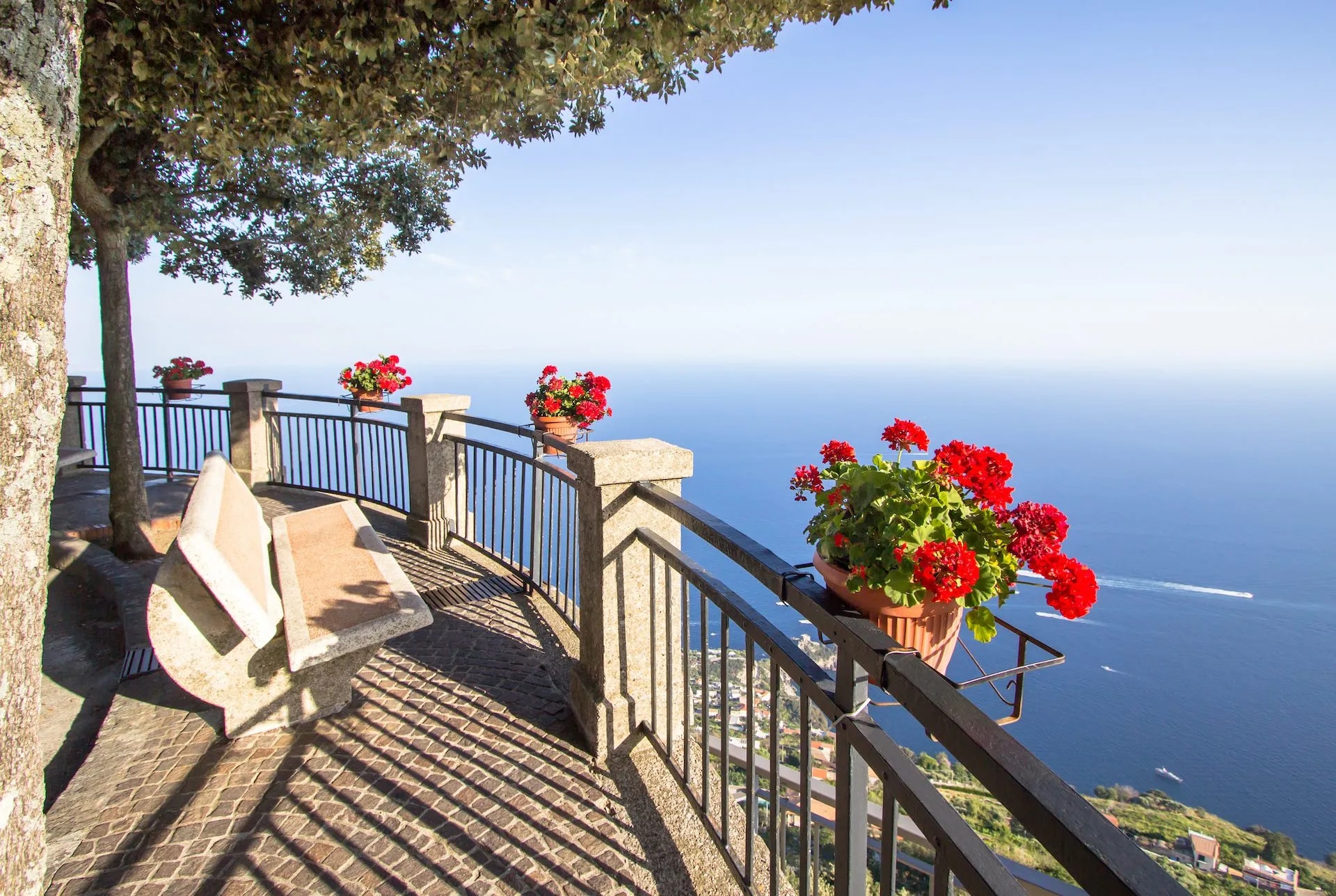 Scenic overlook with stone bench, red geraniums, and deep blue sea view from high above the coast.