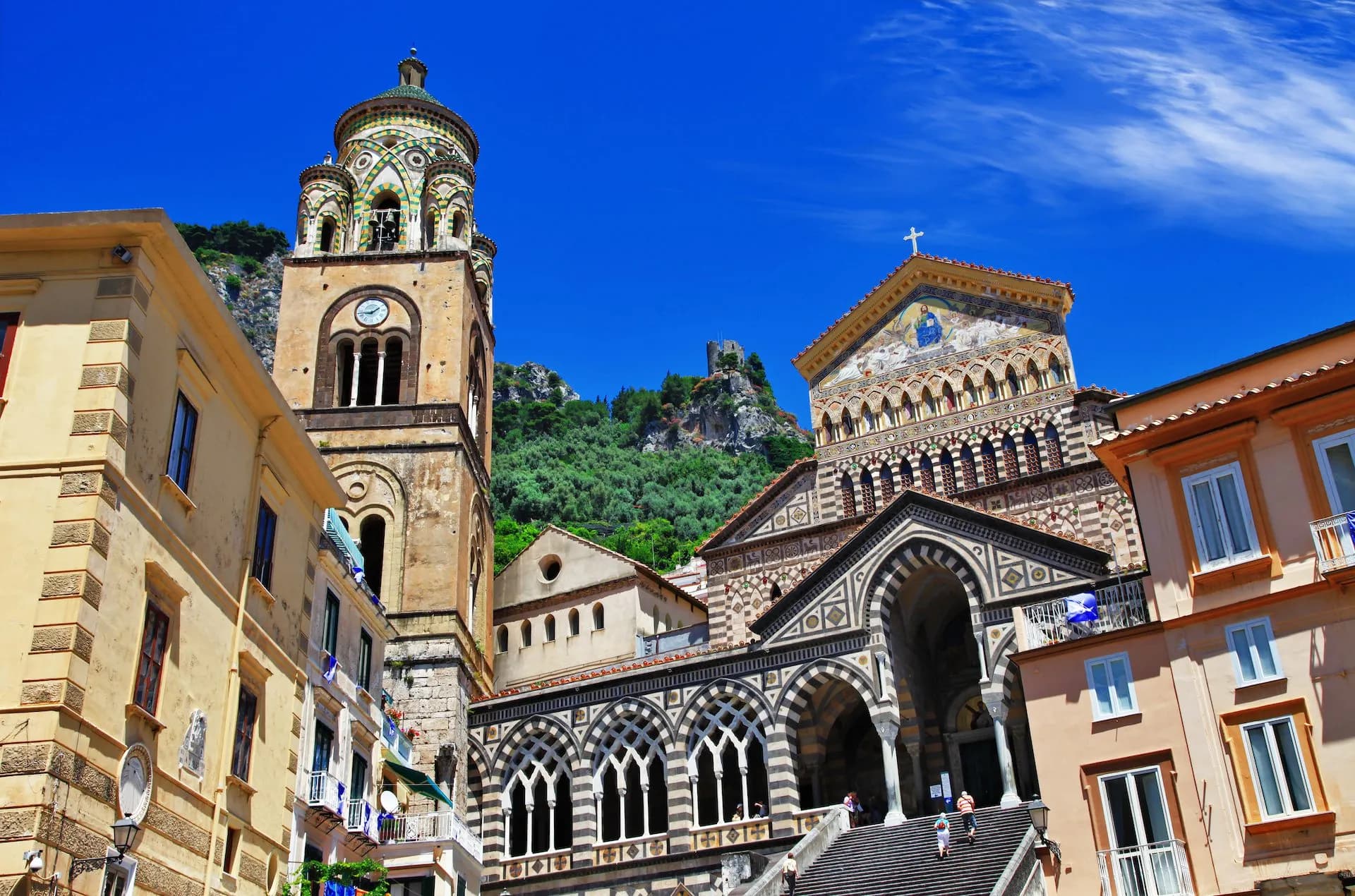 Cathedral of St. Andrea with bell tower, colorful facade, and steep steps under bright blue sky.