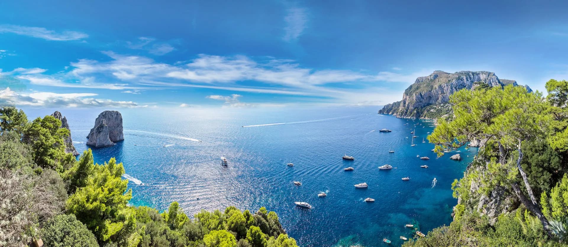 Boats on deep blue sea near rocky cliffs and green foliage on Capri Island.