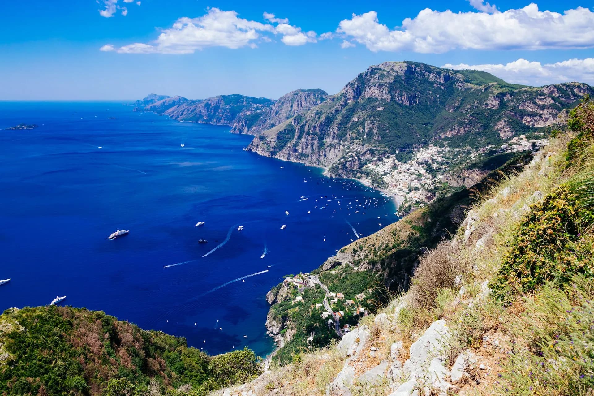 Hiking view of Positano and Amalfi Coast from Sentiero degli Dei over blue sea with boats.