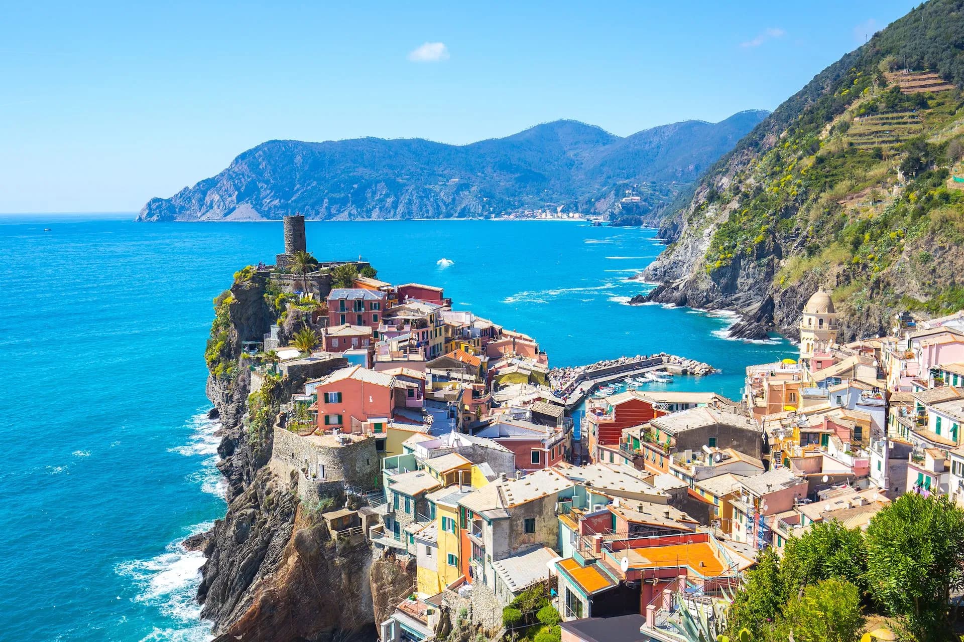 Colorful cliffside village of Vernazza overlooking bright blue Mediterranean Sea and steep green hills.