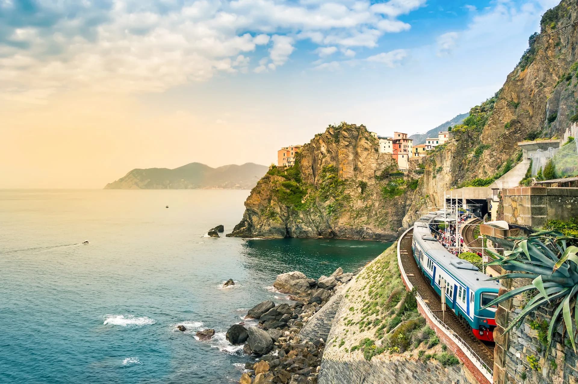 Train arriving at Manarola station along the rugged Mediterranean coastline with colorful buildings.