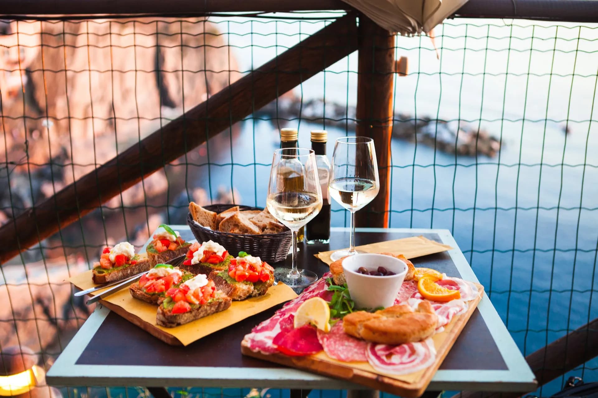 Bruschetta, charcuterie, and white wine dining outdoors overlooking the sea in Manarola.