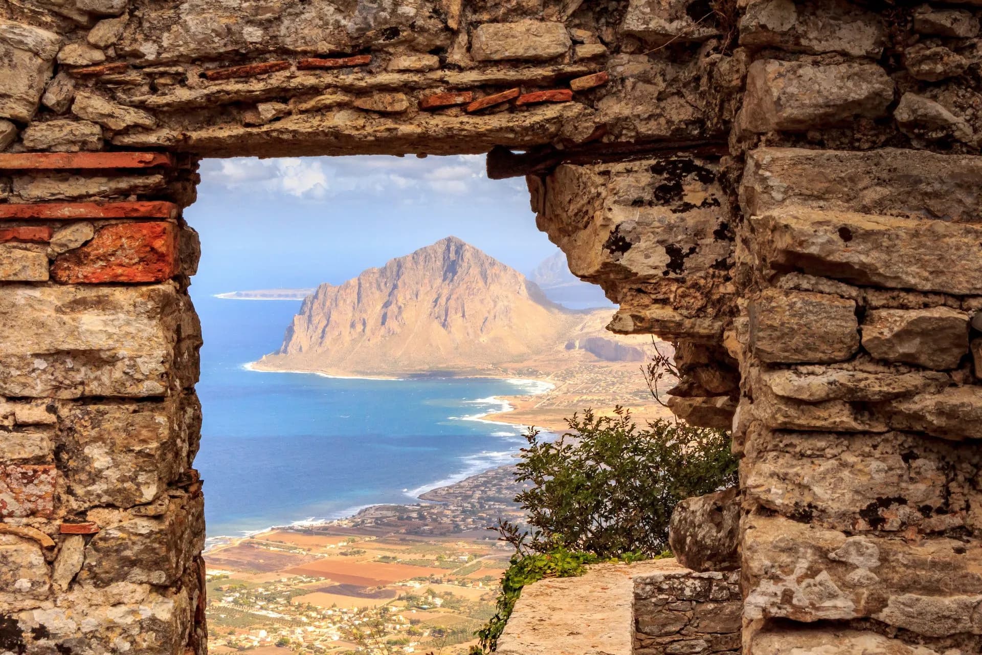 View through stone window frame of Monte Cofano and Mediterranean coastline near Erice.