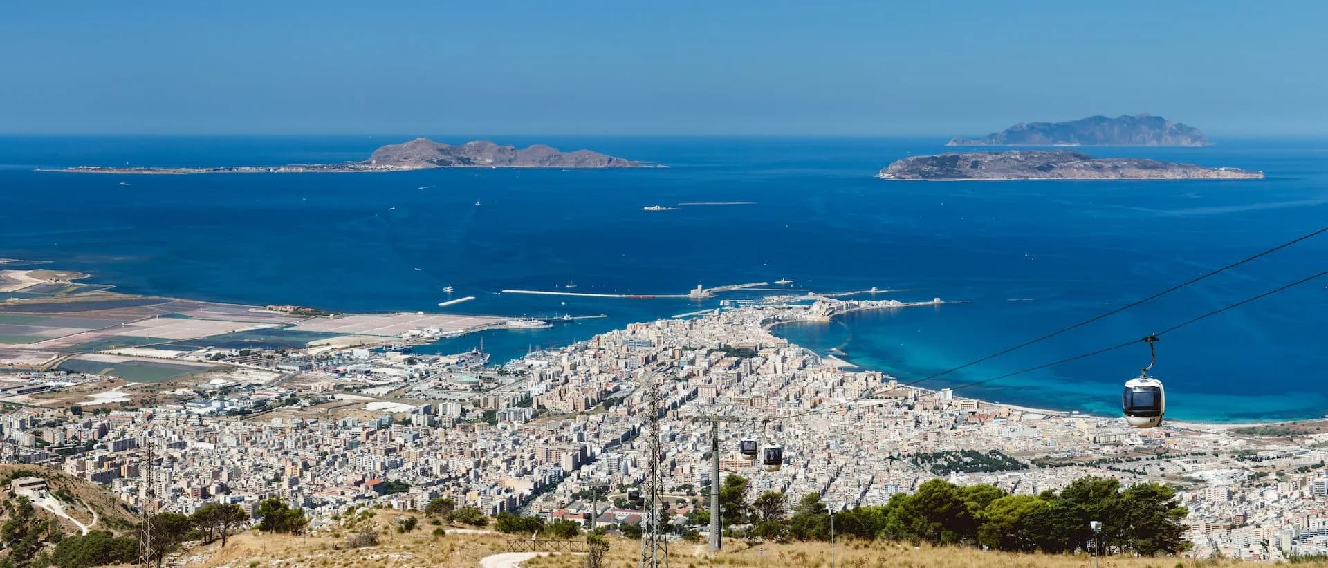 Cable car descending over Trapani city, harbor, and Egadi Islands in the blue sea.